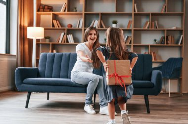 Arkasında hediye kutusu tutan kız. İyi tatiller. Genç anne kızıyla birlikte dairede..