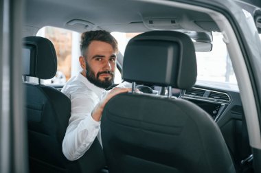 Arkana bak. Beyaz elbiseli genç adam araba galerisinde..