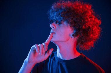 Kırmızı ve mavi renkler. Kıvırcık saçlı genç adam kapalı alanda neon ışıkla aydınlatılır..