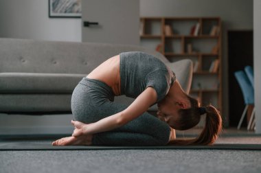 Esneme egzersizine odaklan. Yoga elbiseli genç bir kadın içeride spor yapıyor..