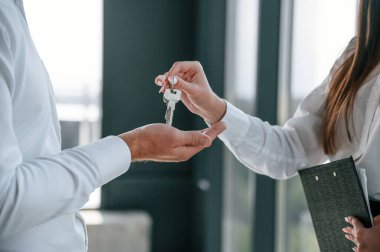 Manzarayı kapat. Mutlu genç bayan yeni evinin anahtarlarını içeride alıyor. Resmi giyinmiş bir adamla..