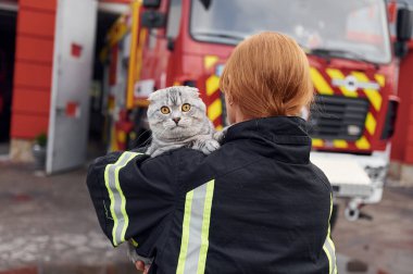 Arkadan bak. Kediyi omuzlarında tutarak. Üniformalı kadın itfaiyeci departmanda çalışıyor..