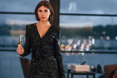 Şampanya tutuyorum. Siyah elbiseli güzel bir kadın yeni yıl partisinde pencerenin yanında duruyor..
