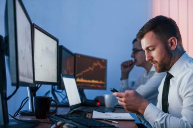 Akıllı telefonu elinde tutarak. Ofiste değişim teknolojisiyle çalışan iki borsacı..