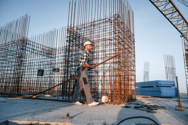 Büyük metal nesnelerin yanında. Gündüz vakti inşaatta çalışan bir adam var..