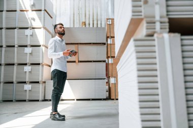 Yönetici tablet kullanarak verileri kontrol ediyor. Depo işçisi depoda bir sürü ürünle birlikte..