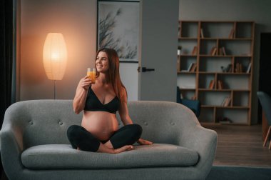 Kanepede oturup portakal suyu içmek. Güzel hamile kadın evde..