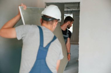 İnşaat parçalarını elle taşımak. İki adam dairede birlikte tamirat yapıyor..