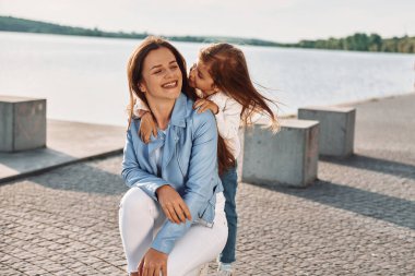 Birbirinize sarılıp gülümsüyorsunuz. Genç anne ve kızı yazın göl kenarında eğleniyorlar..