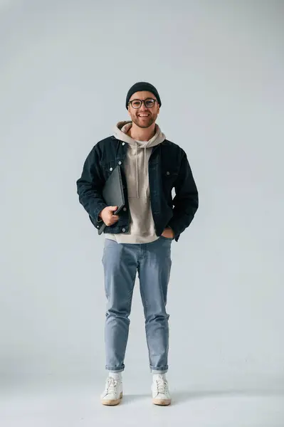 stock image IT specialist in hat and glasses standing with laptop. Handsome man is in the studio against white background.