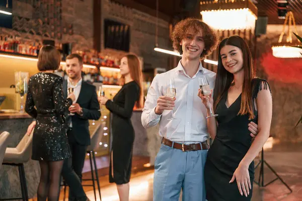 stock image Man with woman is standing and posing. Group of people in beautiful elegant clothes are celebrating New Year indoors together.