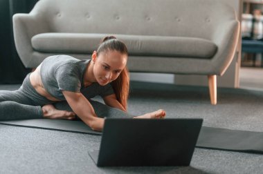Laptop kullanıyorum. Yoga elbiseli genç bir kadın içeride spor yapıyor..