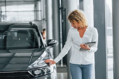 Tablet ellerde. Kıvırcık sarı saçlı kadın otosalonda..