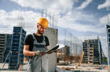 Sürecin kontrolü. Foreman belgelerle birlikte. Üniformalı adam inşaat alanında çalışıyor..