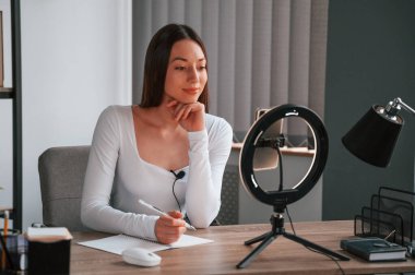 Akıllı telefon kullanarak güzellik ustası sınıfı. Beyaz elbiseli genç ve güzel bayan ofiste..