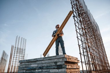 Gri üniformalı. Tahta tutuyorlar. Gündüz vakti inşaatta çalışan bir adam var..