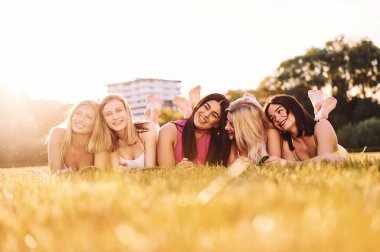 Yere yatıp gülümsüyor. Bir grup kadın sahada birlikte spor yapıyorlar..