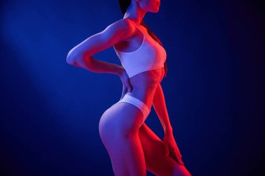 Yan görüş. İç çamaşırlı genç kadın stüdyoda neon ışıklarıyla bekliyor..