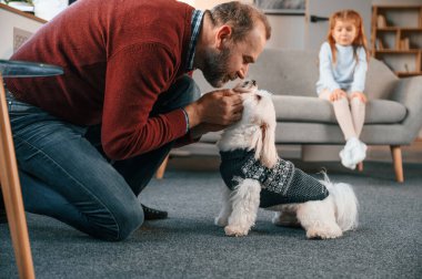Adam Malta 'lı köpeğine bakıyor. Kız kanepede oturuyor..
