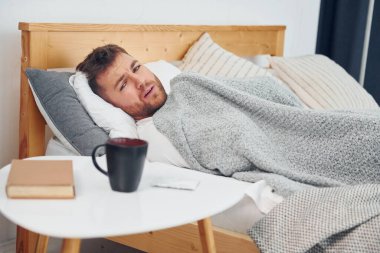 Hasta adam evde yatağa uzanmış ve kendini kötü hissediyor. Kişisel izolasyon kavramı.