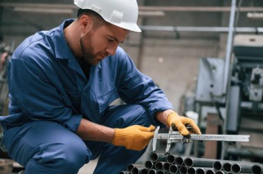 Metal boruyu ölçmek için Calliper kullanıyor. Mavi üniformalı fabrika işçisi içeride..