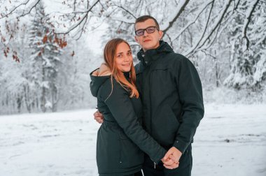 Birbirini kucaklarken durup poz vermek. Çift kış ormanında yürüyüş yapıyor..