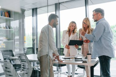 Büyük pencerelere yaslan. Profesyonel iş adamlarından oluşan bir grup ofiste..