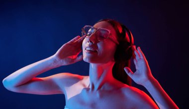 Kulaklık kullanarak müziğin tadını çıkarıyorum. İçerideki neon ışıkta duran genç bir kadının portresi..