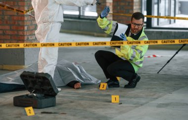 Kadın elinde tabancayla onu tehdit ederken, polis memuru cesedin yanında oturuyor..