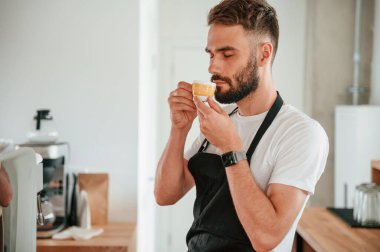 Lezzetli kahve tadı. Beyaz gömlekli ve siyah önlüklü kafe çalışanı içeride..