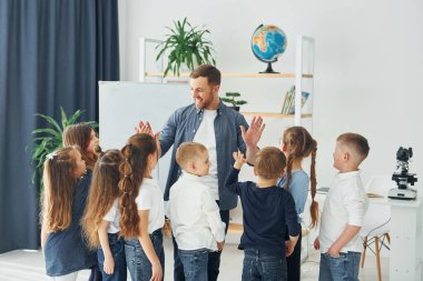 Dersin sonunda beşlik çakıyorsun. Okulda öğretmenle birlikte bir grup çocuk öğrenci..