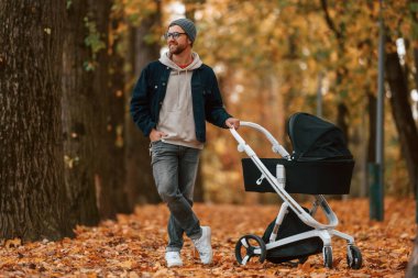 Ön manzara. Bebek arabalı adam sonbahar parkında yürüyüş yapıyor..