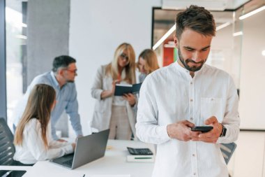 Kameraya poz veren güzel, neşeli bir adam. Profesyonel iş adamlarından oluşan bir grup ofiste..