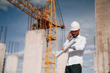 Telefonla konuşmak ve belgeleri elinde tutmak. Üniformalı adam inşaat alanında çalışıyor..
