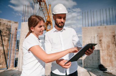 Not defterindeki belgeyi okuyorum. Üniformalı bir adam inşaat alanında kadınla çalışıyor..