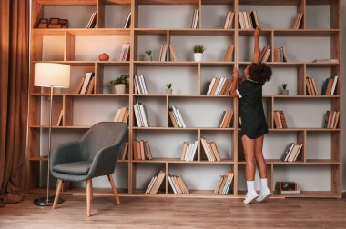 Raflardaki kitaplara bakınıyorum. Okul üniformalı tatlı Afro-Amerikan kız kütüphanede..