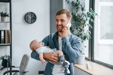 Telefonla konuşuyorlar. Yürüyen bebekle baba içeride, ofiste..