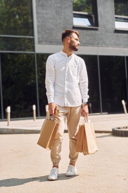 Modern binanın yanında duruyor. Şık genç adamın alışveriş günü var. Çantalarla dışarıda..