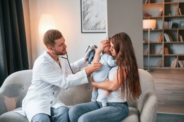 Steteskop kullanıyorum. Erkek doktor, kadının yeni doğan bebeğine evde bakıyor..