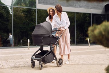 İki bayan arkadaş dışarıda bebek arabasıyla yürüyorlar..