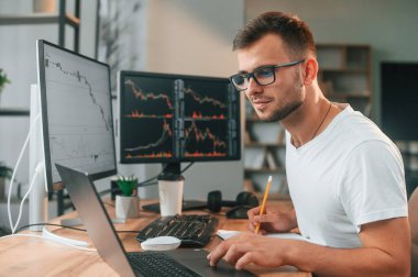 Laptop masanın üstünde. Genç borsacı ofiste bilgisayar kullanarak çalışıyor..