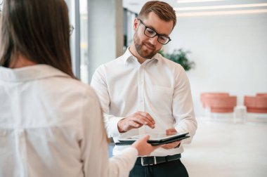 Elinde tabletle. Resmi giyinmiş kadın ve erkek içeride birlikte çalışıyorlar..
