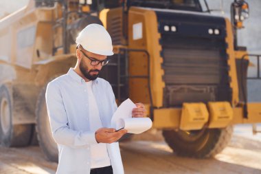 Gözlüklü, doküman okuyor. Üniformalı adam gündüz taş ocağında çalışıyor..