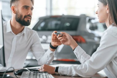 Yeni otomobilin sahibi anahtarlarını alıyor. Beyaz elbiseli bir adam araba galerisinde birlikte..