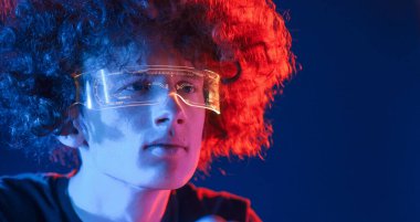 Fütürist gözlük. Kıvırcık saçlı genç adam kapalı alanda neon ışıkla aydınlatılır..