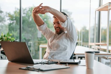 Kulaklıkla dizüstü bilgisayar başında oturmak. Resmi kıyafetli adam modern ofiste çalışıyor..