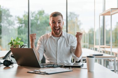 Başarıyı kutluyoruz. Resmi giyinmiş mutlu adam modern ofiste çalışıyor..