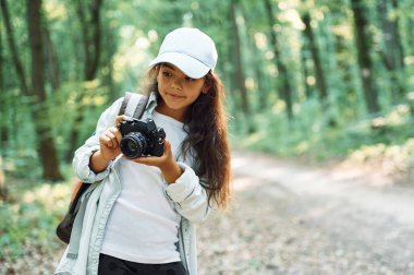 Ayakta ve kamerayı elinde tutarak. Kız yaz günü ormanda yeni yerler keşfediyor..