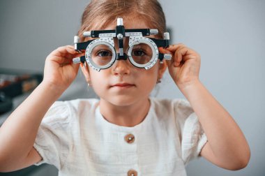 Lensleri olan özel bir cihazla. Küçük kız, kadın doktorun yardımıyla klinikte görüşünü kontrol ediyor..