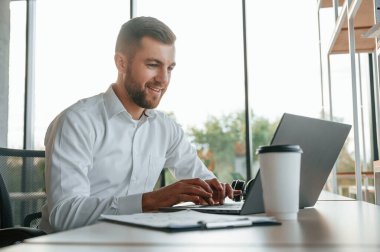 Laptop kullanıyorum. Resmi kıyafetli adam modern ofiste çalışıyor..